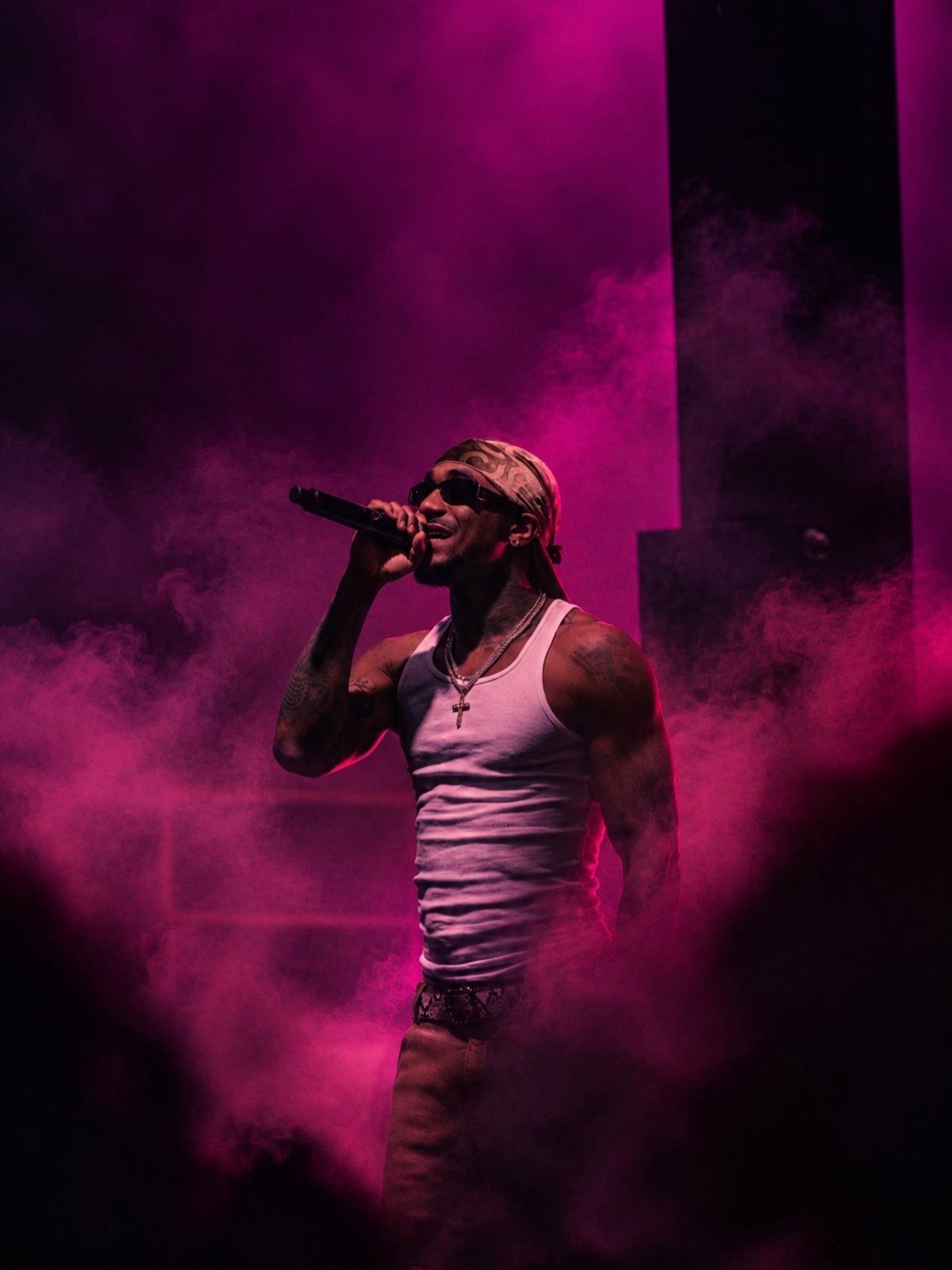 Performer in sunglasses and a tank top singing through pink stage smoke